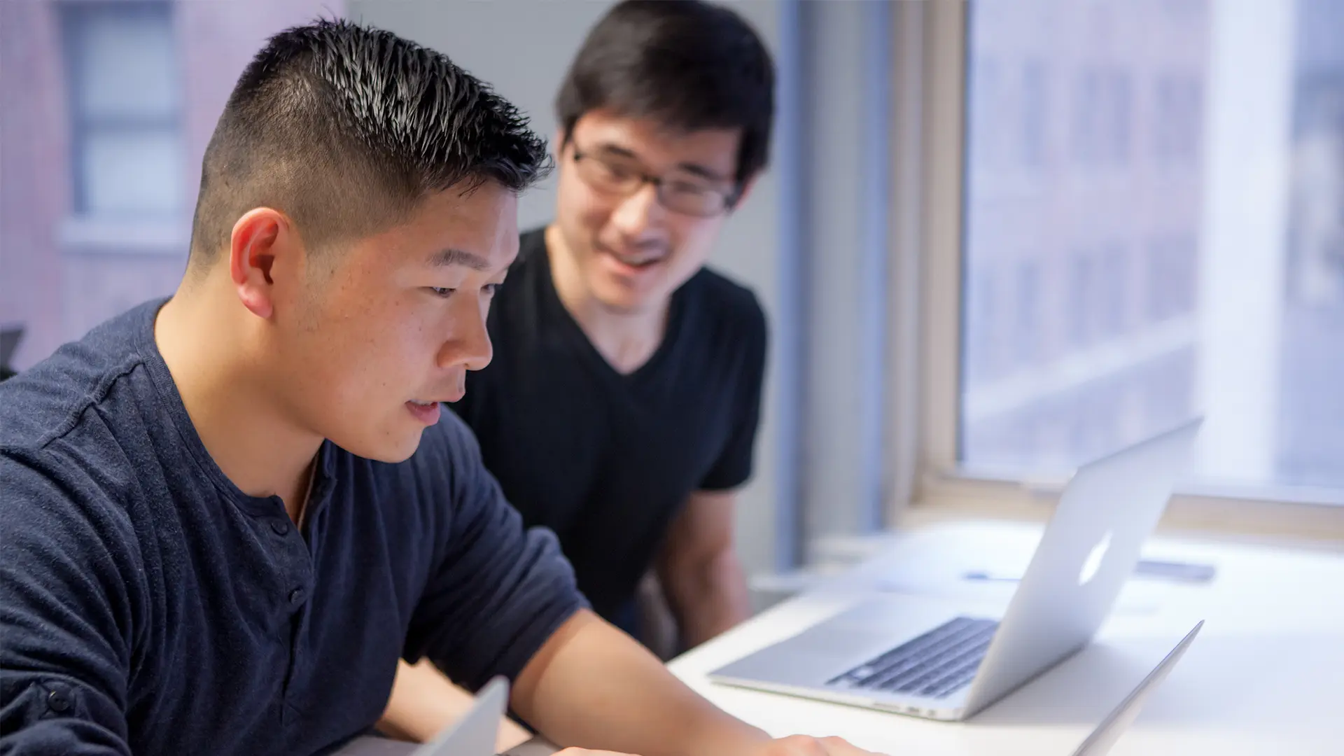 Two students working together on laptops during a business English class.