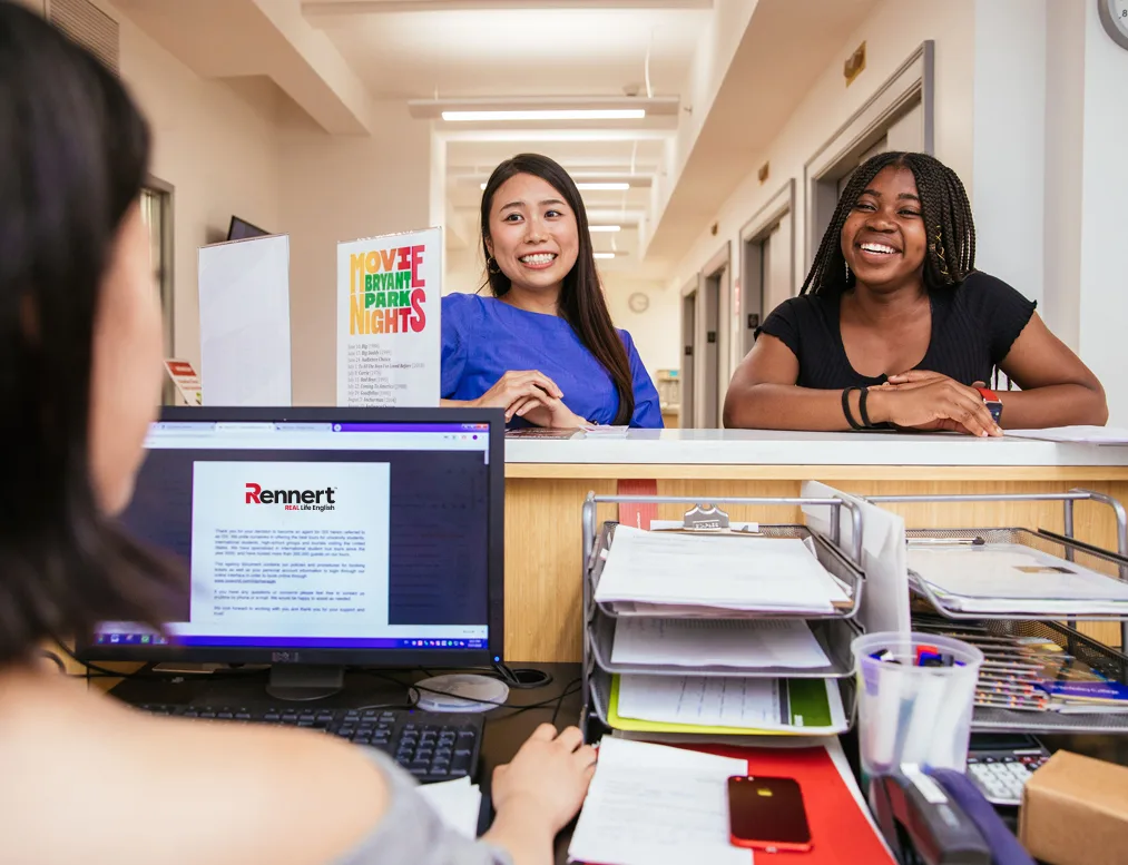 Person at the front desk of Rennert School talking with two students.